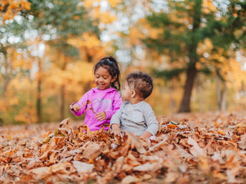 Cute siblings playing while sitting on autumn leaf in forest