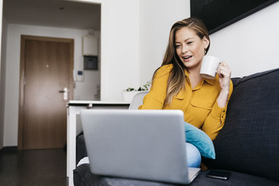 Low angle view of young woman using laptop on sofa at home