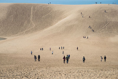 People on sand dune against clear sky