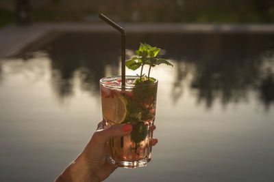 Close-up of hand holding drink against water