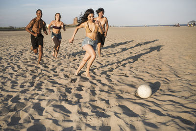 Happy friends playing soccer at beach on sunny day