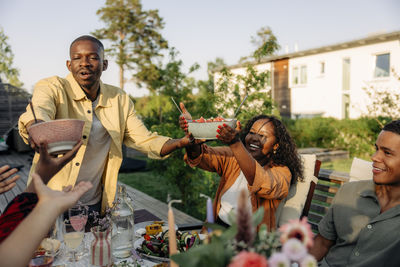 Young man serving food to friends during dinner party in back yard