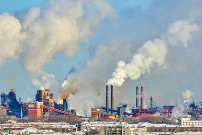 Smoke emitting from factory against cloudy sky