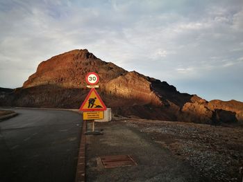 Road sign by mountains against sky