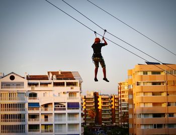 Low angle view of man jumping against buildings in city