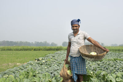 Portrait of farmer holding basket of vegetable at farm land