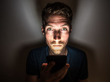 Portrait of young man using phone while sitting in darkroom
