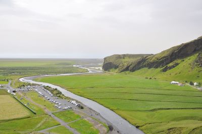 Scenic view of green field by sea against sky