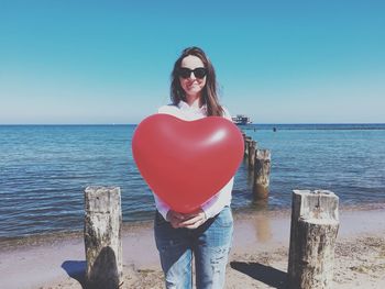 Woman holding heart shape balloon at beach