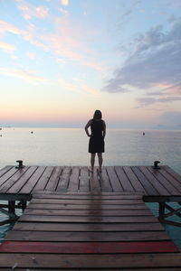 Rear view of woman standing on sea against sky during sunset