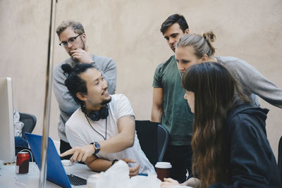 Male computer programmer showing laptop to colleagues in office