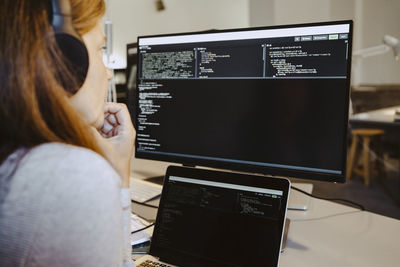 Female hacker looking at codes over computer screen in creative office