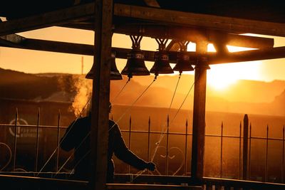 Man ringing bells against sky during sunset