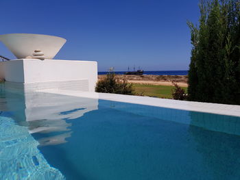 Swimming pool by sea against clear blue sky