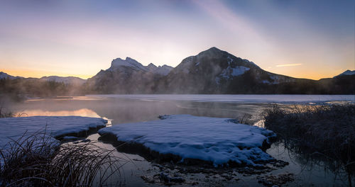Scenic view of frozen lake by mountains against sky during sunset