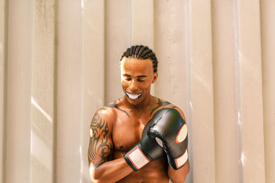 Shirtless man wearing boxing glove while standing against wall