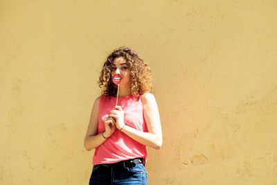 Portrait of young woman holding prop while standing against wall