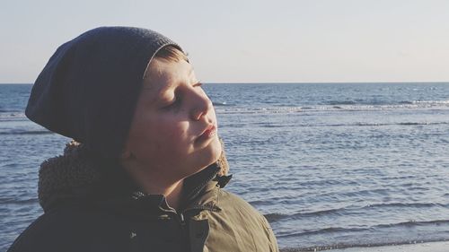 Close-up of boy standing by sea against clear sky