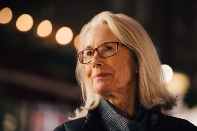 Wrinkled smiling woman looking away while standing in city at night