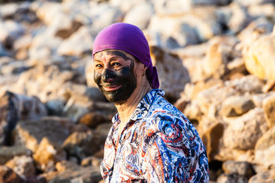 Portrait of senior woman with mud facial mask at rocky shore