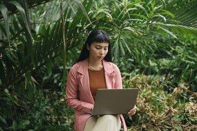 Young woman using phone while standing on plants