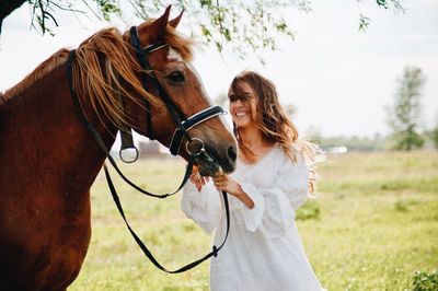 Smiling woman with horse standing on field