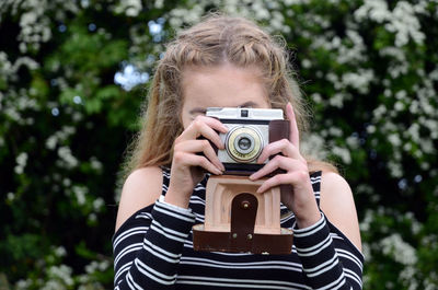 Close-up of woman photographing with vintage camera against trees