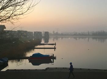 Man standing on boat in lake against sky during sunset