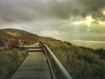 Boardwalk leading towards sea against sky