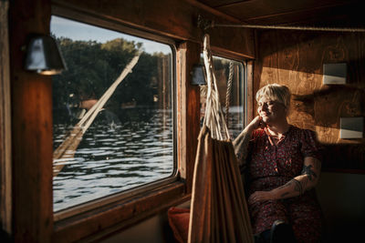 Smiling woman sitting with eyes closed by window on boat