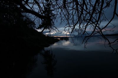 Silhouette trees by lake against sky