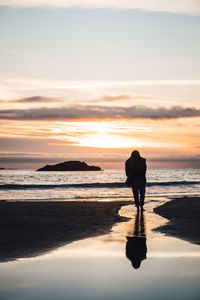 Silhouette man standing on beach against sky during sunset