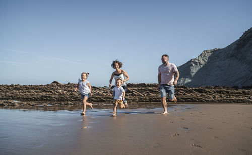 Playful family running at beach against blue sky