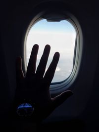 Cropped image of hand against sky seen through airplane window