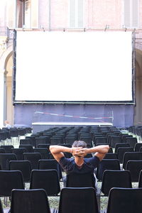 Rear view of man sitting against projection screen on chair