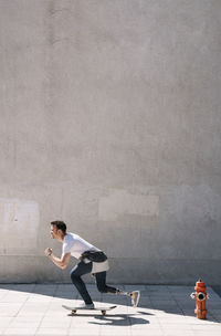 Side view of young guy with leg prosthesis pushing from ground and riding skateboard against concrete wall on city street