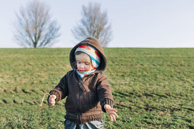 Girl holding plant while standing on grass against sky