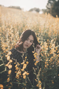 Thoughtful young man standing amidst yellow flowers on field