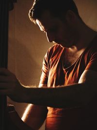 Close-up of man holding guitar against wall at home