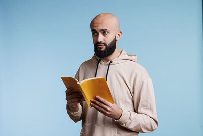 Portrait of young man wearing hat while standing against blue background