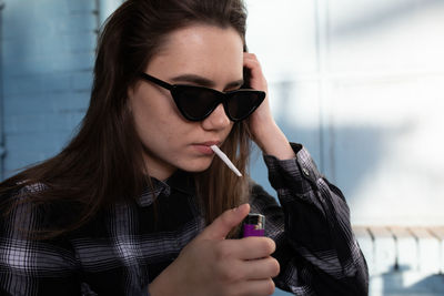 Young woman igniting cigarette while wearing sunglasses