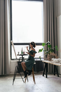 Side view of woman painting on canvas at art studio