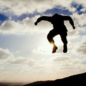 Low angle view of man jumping against cloudy sky