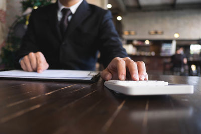 Midsection of man with calculator and paper working at table in cafe