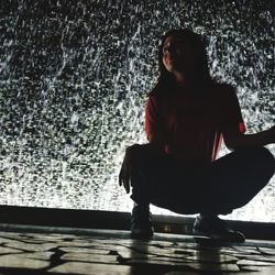 Portrait of young woman sitting against wall