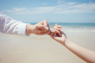 Midsection of couple hands on beach against sky