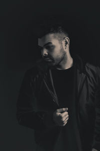 Portrait of young man standing against black background