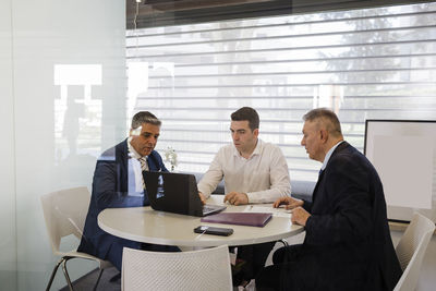 Businessman discussing over laptop with colleagues sitting at desk in office