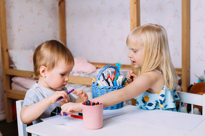 Two little cute blonde children are drawing together at the table.