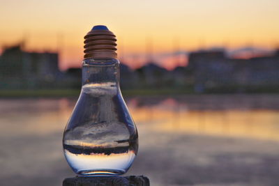 Close-up of water bottle against river during sunset